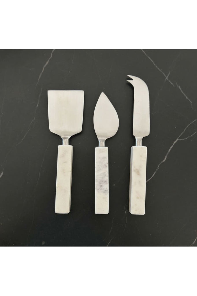Nel Lusso 3 piece Blanco Cheese Knife Set  featuring solid white marble handles and stainless ends.   Set displayed on a black marble borard.
