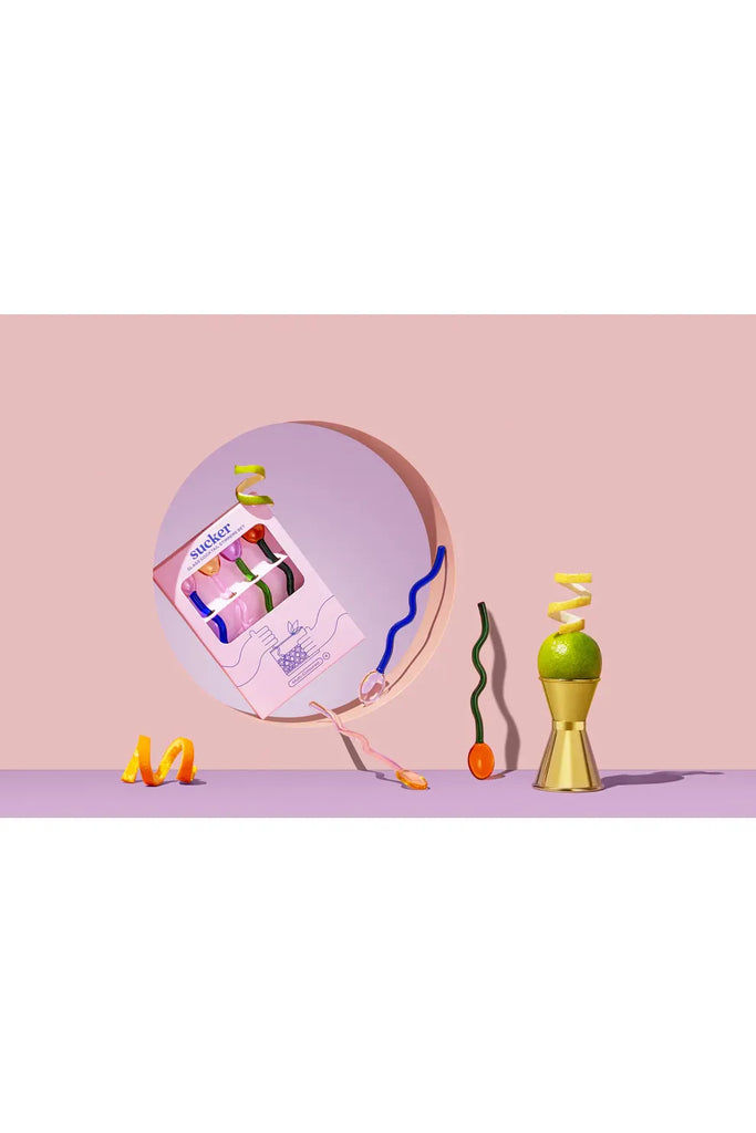 Sucker multicoloured cocktail stirrers and other bar accessories, including a jigger on a pink background.