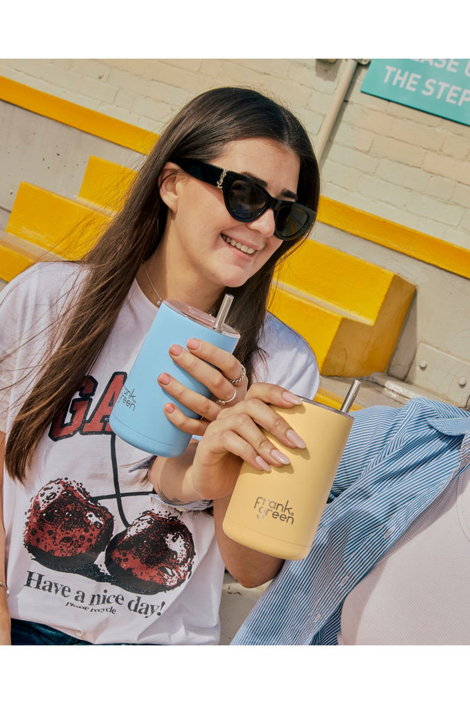 Two Women holding two reusable cups in front of a yellow and white brick wall.