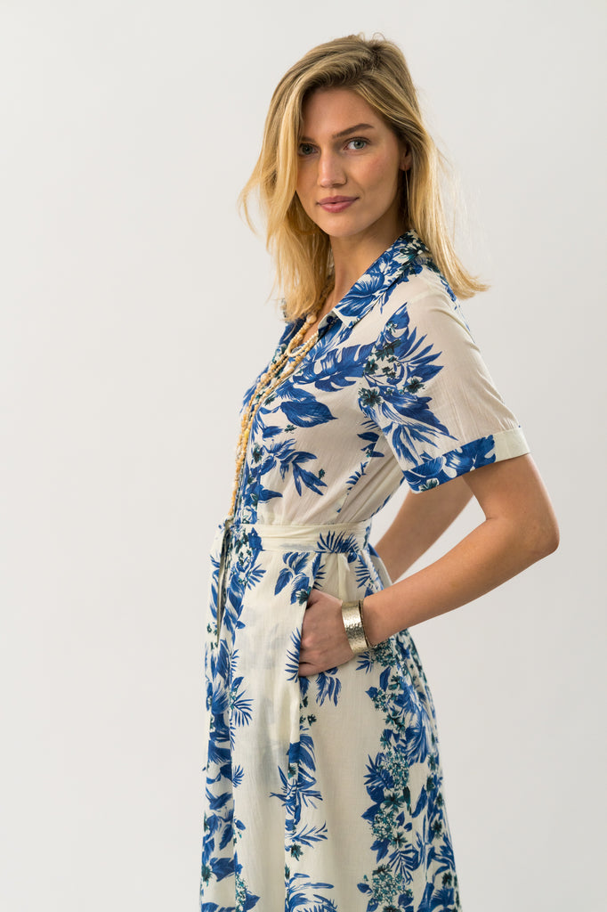 Woman wearing a white dress with blue floral patterns on a plain background