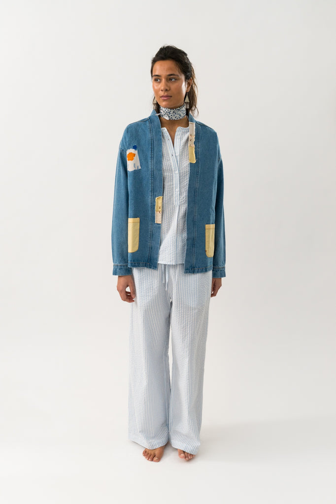 Person wearing a blue denim jacket with patch details on a white background. Lollys Laundry Mila Jacket washed denim.