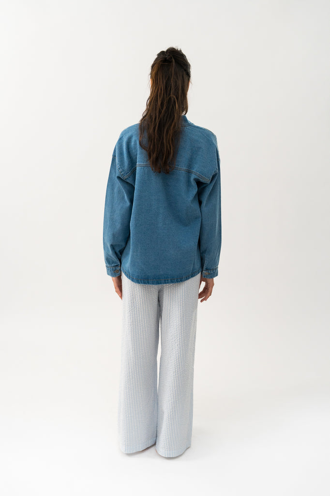 Person wearing a blue denim jacket with patch details on a white background. Lollys Laundry Mila Jacket washed denim.