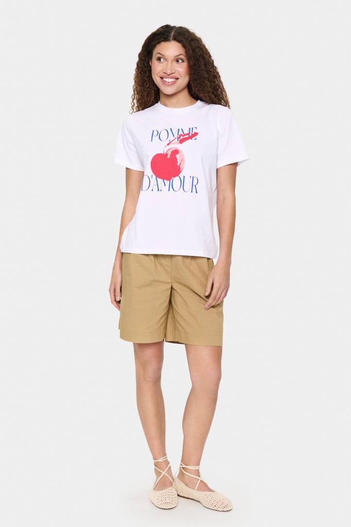 Woman wearing a white t-shirt with a graphic design and beige shorts on a white background. Saint Tropez Harda Tee in white.