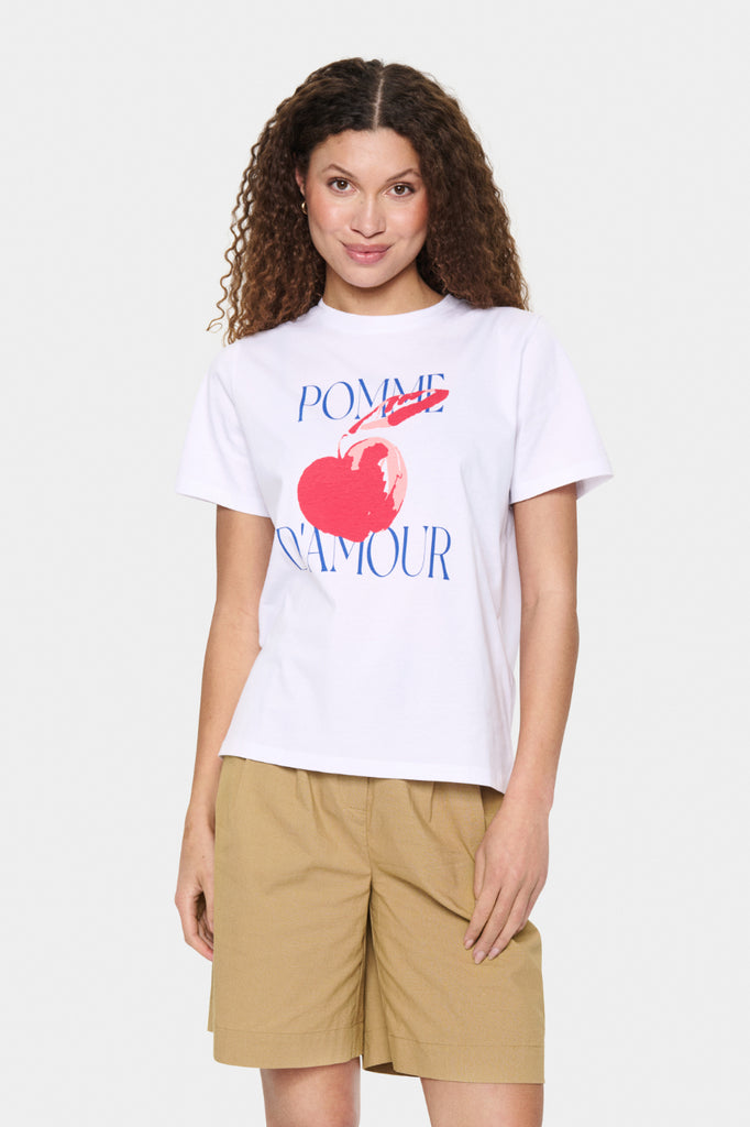 Woman wearing a white t-shirt with a graphic design and beige shorts on a white background. Saint Tropez Harda Tee in white.