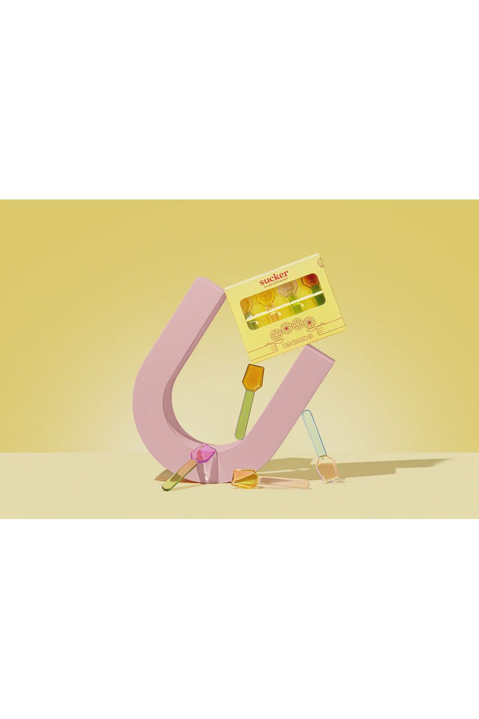 Sucker Multicoloured Set of 4 Glass Spoons. Pink U-shaped holding Sucks packaged multicoloured Glass Spoon Set on a yellow background.