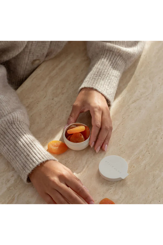Person holding a mini Styleware bowl filled with dried apricots on a light surface.