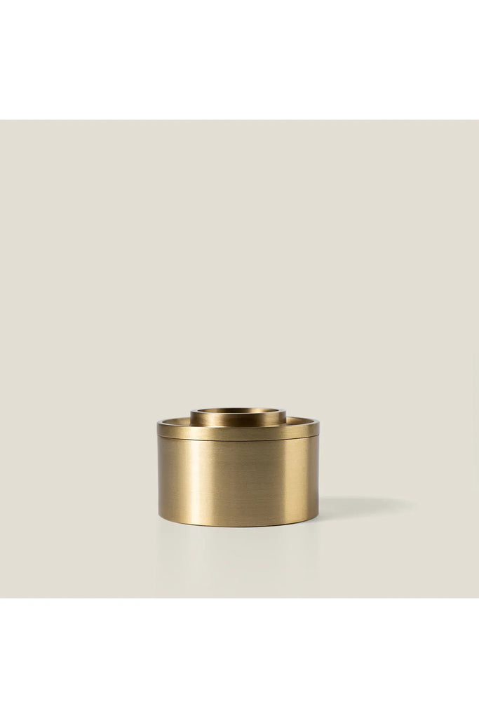 Addition Studion Asteroid Brass Oil Burner. Gold cylindrical container on a beige background.