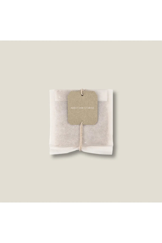 Addition Studio Giant Tea Bag for the Bath Brew. Mesh teabag with a tag on a beige background.