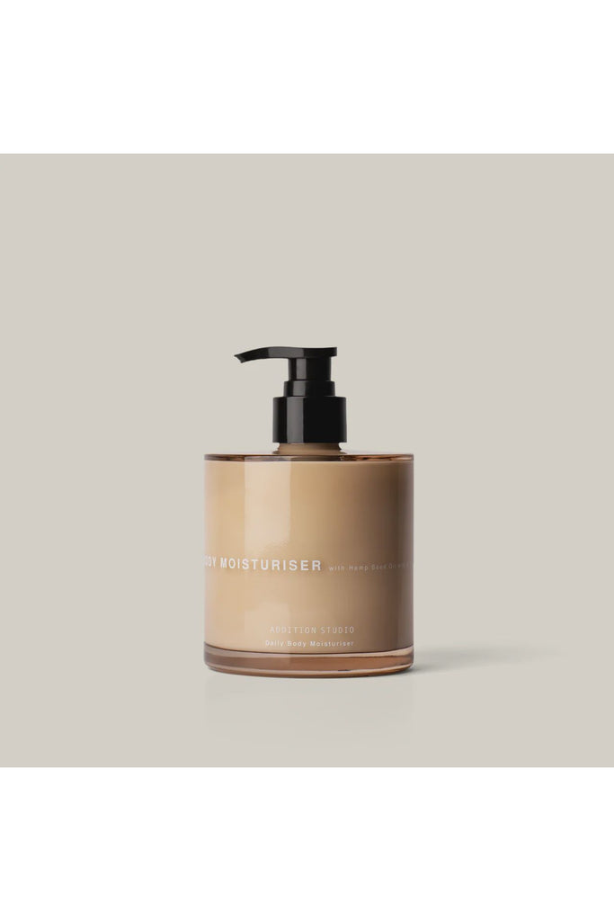 Addition Studio Daily Body moisturiser. Glass Bottle with a Black Pump of moisturiser on a light grey background.