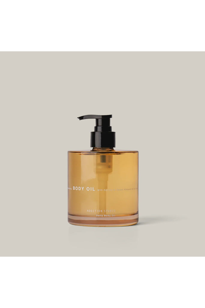 Addition Studio Daily Body Oil. Amber glass bottle with pump labelled 'Body Oil' on a beige background.