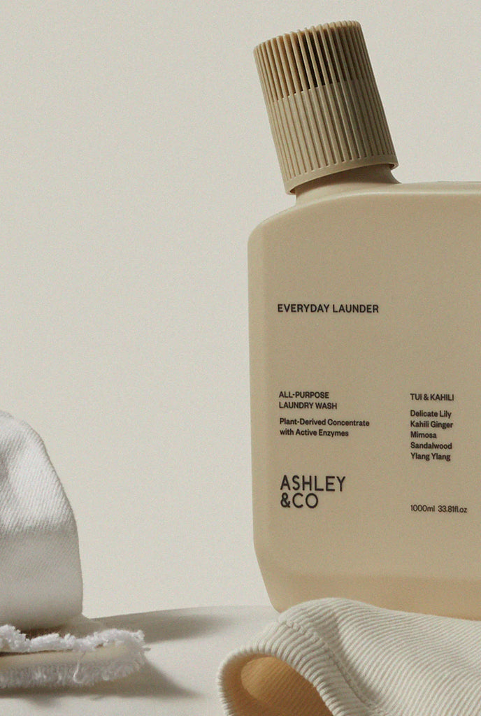 ASHLEY & CO EVERYDAY LAUNDER ALL PURPOSE LIQUID LAUNDRY DETERGENT BOTTLE SITTING ON LAUNDRY BENCH AMONGST WASHING.