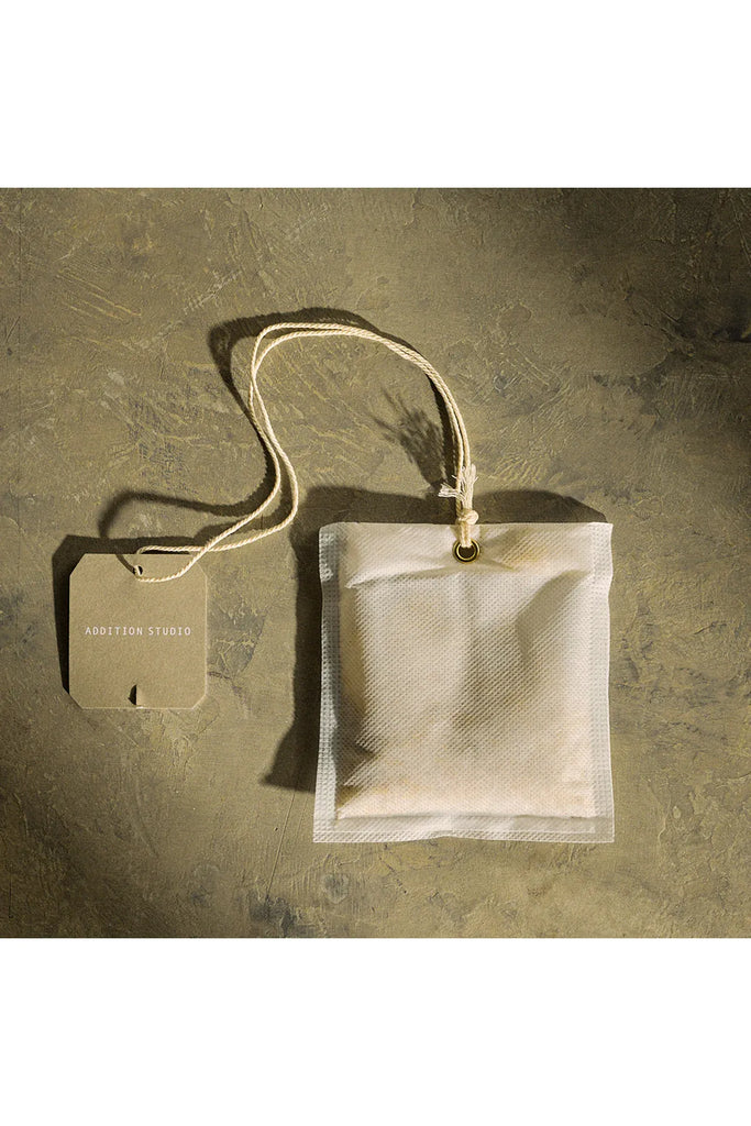 Addition Studio Giant Tea Bag for the Bath Brew. Mesh teabag with a handle on a textured brown surface.