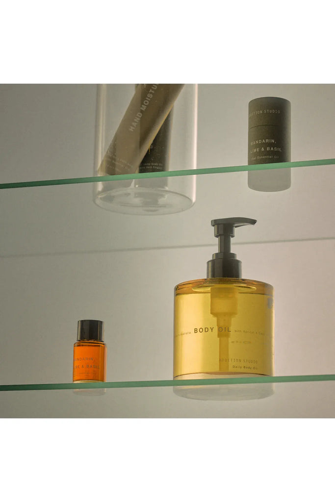 Glass shelf with Addition Studio body oil bottle and other products sitting on the shelf.