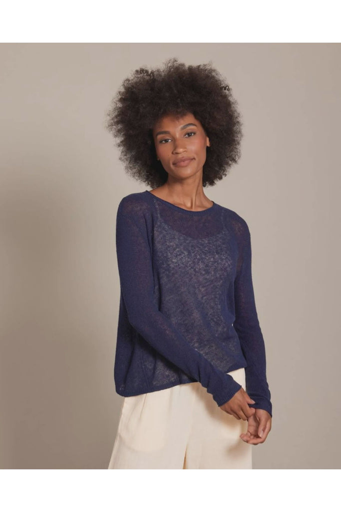 Woman wearing a blue sweater and white pants against a beige background. Alashan Seed Stitch Crew Neck Jumper in Stargazer.