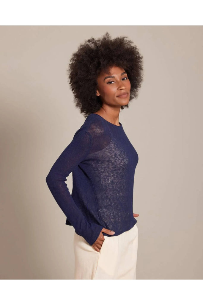 Woman wearing a blue sweater and white pants against a beige background. Alashan Seed Stitch Crew Neck Jumper in Stargazer.