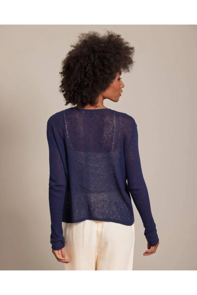 Woman wearing a blue sweater and white pants against a beige background. Alashan Seed Stitch Crew Neck Jumper in Stargazer.