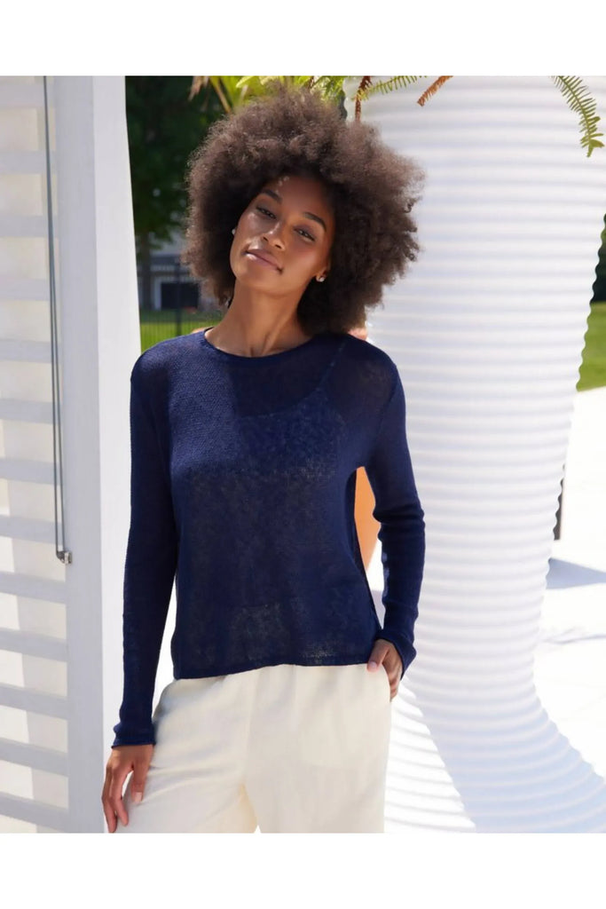Woman wearing a blue sweater and white pants against a beige background. Alashan Seed Stitch Crew Neck Jumper in Stargazer.