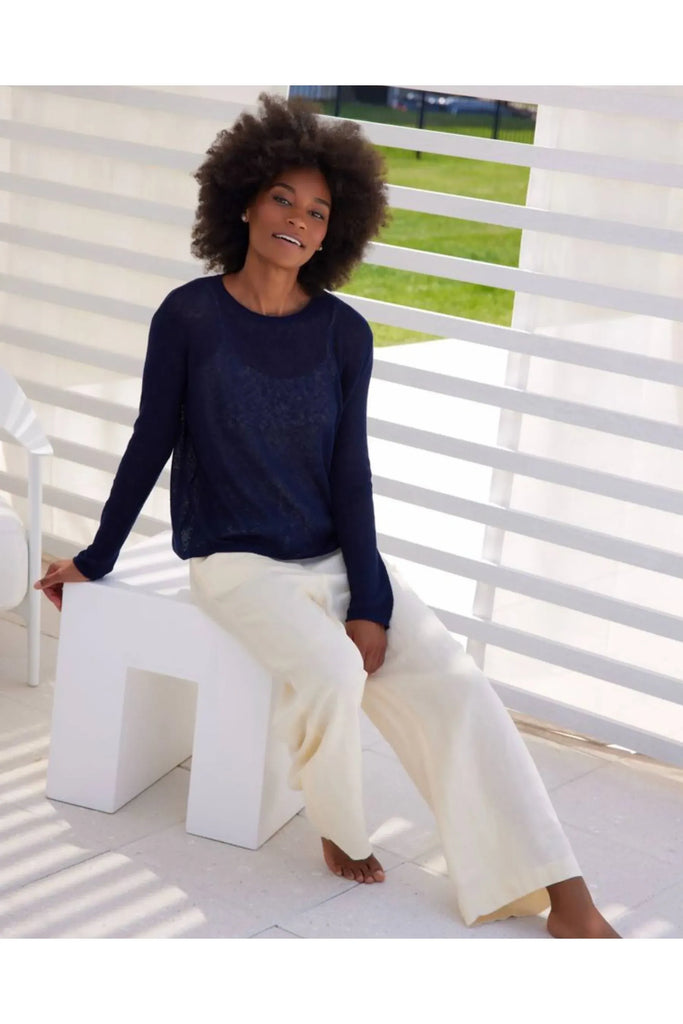 Woman wearing a blue sweater and white pants against a beige background. Alashan Seed Stitch Crew Neck Jumper in Stargazer.