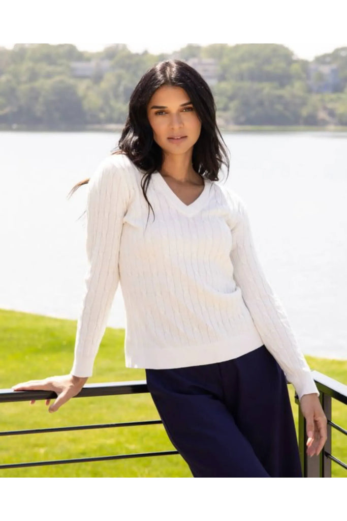 Woman wearing a white sweater standing by a lake with greenery in the background. Alashan White April v Neck Cable Jumper