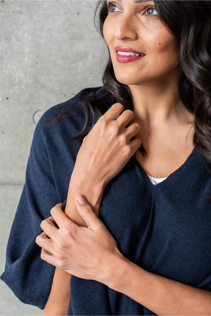 Woman wearing a navy blue poncho over a white top and pants on a white background. Alashan Cotton Cashmere Topper in French Navy.