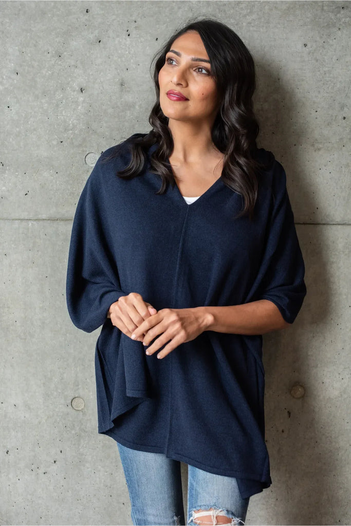 Woman wearing a navy blue poncho over a white top and pants on a white background. Alashan Cotton Cashmere Topper in French Navy.