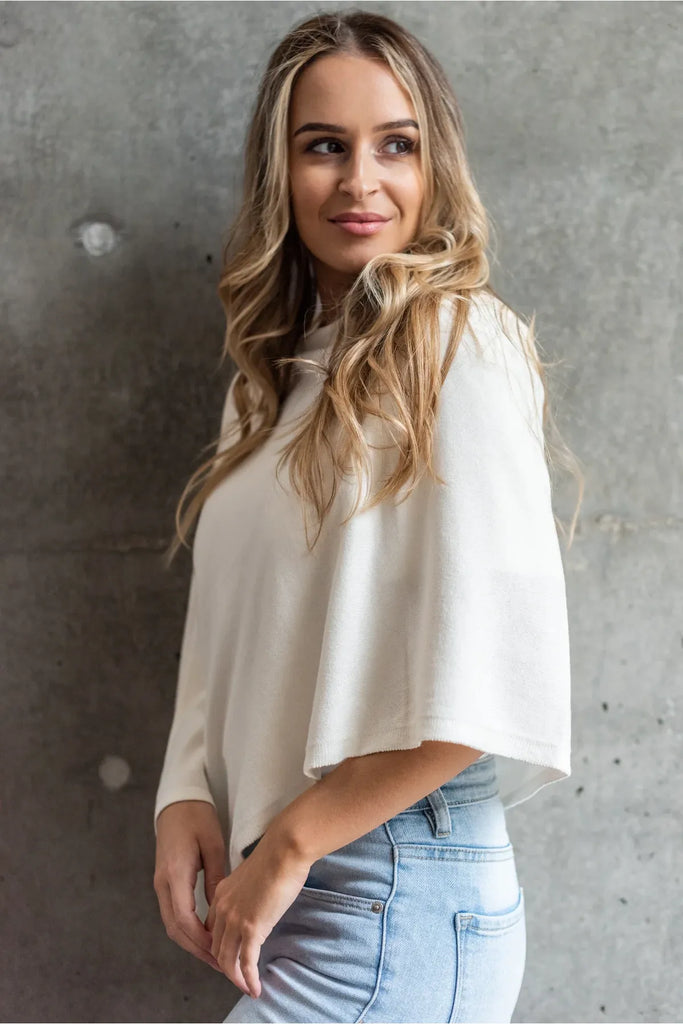 Woman wearing a white shawl over a white top and pants on a white background. Alashan Cotton Cashmere Topper in Off White.