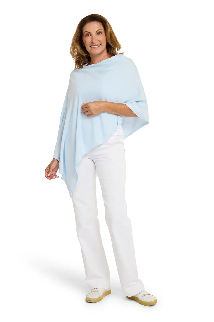 Woman wearing a light blue poncho over a white outfit on a white background. Alashan Cotton Cashmere Topper in Rain blue.