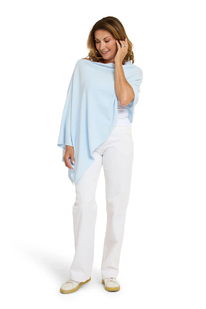 Woman wearing a light blue poncho over a white outfit on a white background. Alashan Cotton Cashmere Topper in Rain blue.