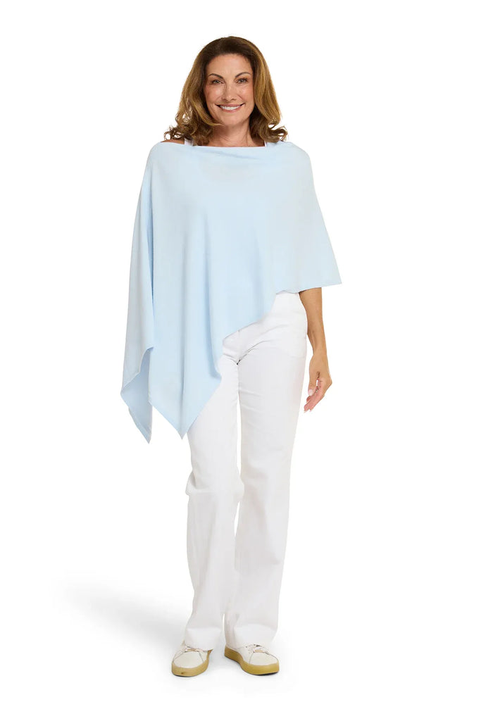 Woman wearing a light blue poncho over a white outfit on a white background. Alashan Cotton Cashmere Topper in Rain blue.