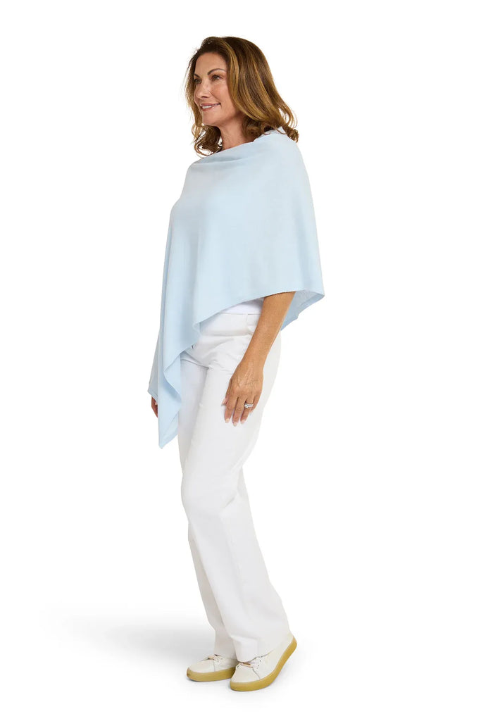 Woman wearing a light blue poncho over a white outfit on a white background. Alashan Cotton Cashmere Topper in Rain blue.