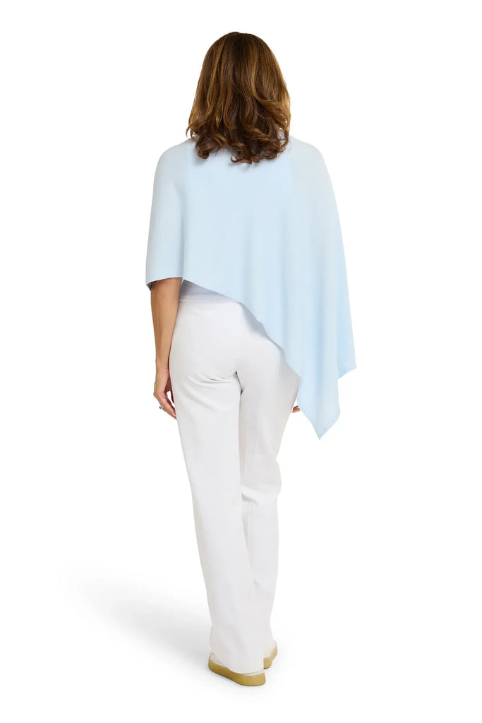 Woman wearing a light blue poncho over a white outfit on a white background. Alashan Cotton Cashmere Topper in Rain blue.