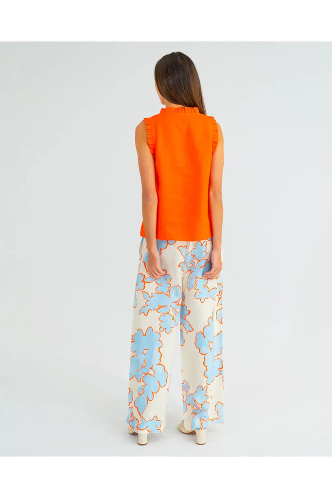 Woman wearing an orange sleeveless top with ruffled details on a plain background. Arlington Milne Lucia Top in Tangerine worn with the Bianca Trouser in Summertime Floral.