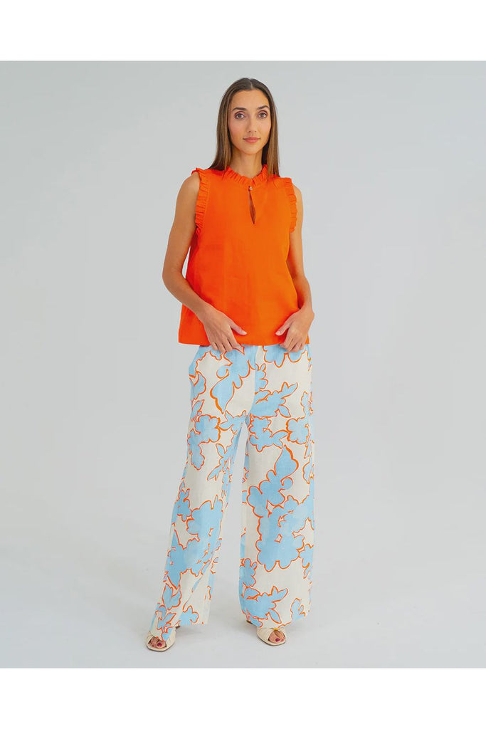 Woman wearing an orange sleeveless top and patterned pants on a gray background. Arlington Milne Bianca trouser in Summertime Floral worn with the Lucia Top in tangerine.