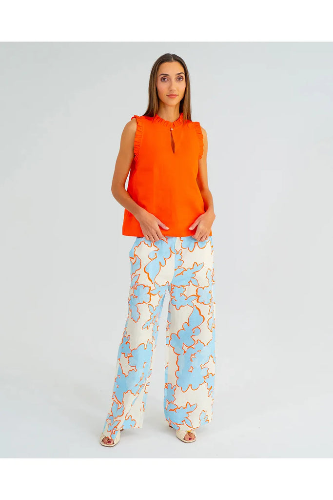 Woman wearing an orange sleeveless top with ruffled details on a plain background. Arlington Milne Lucia Top in Tangerine worn with the Bianca Trouser in Summertime Floral.
