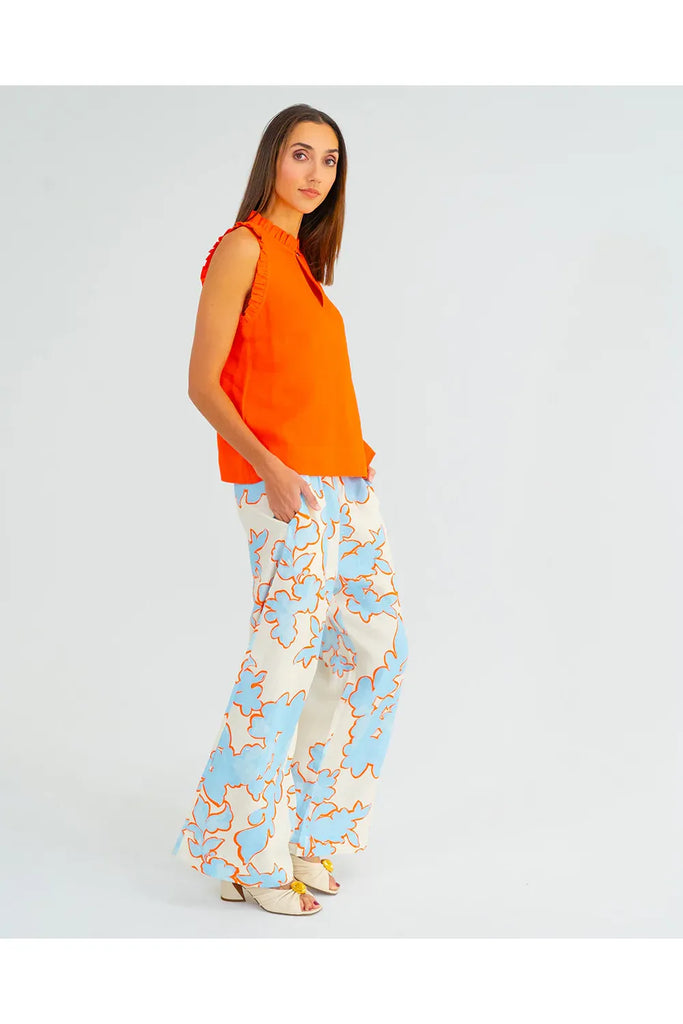 Woman wearing an orange sleeveless top and patterned pants on a gray background. Arlington Milne Bianca trouser in Summertime Floral worn with the Lucia Top in tangerine.