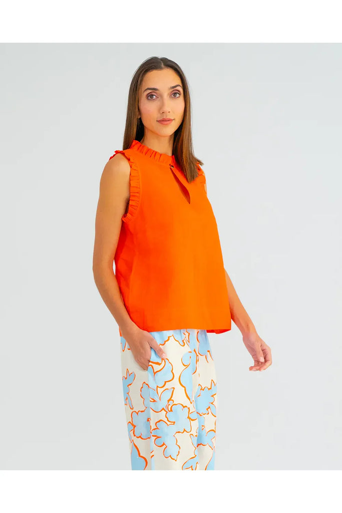 Woman wearing an orange sleeveless top with ruffled details on a plain background. Arlington Milne Lucia Top in Tangerine worn with the Bianca Trouser in Summertime Floral.