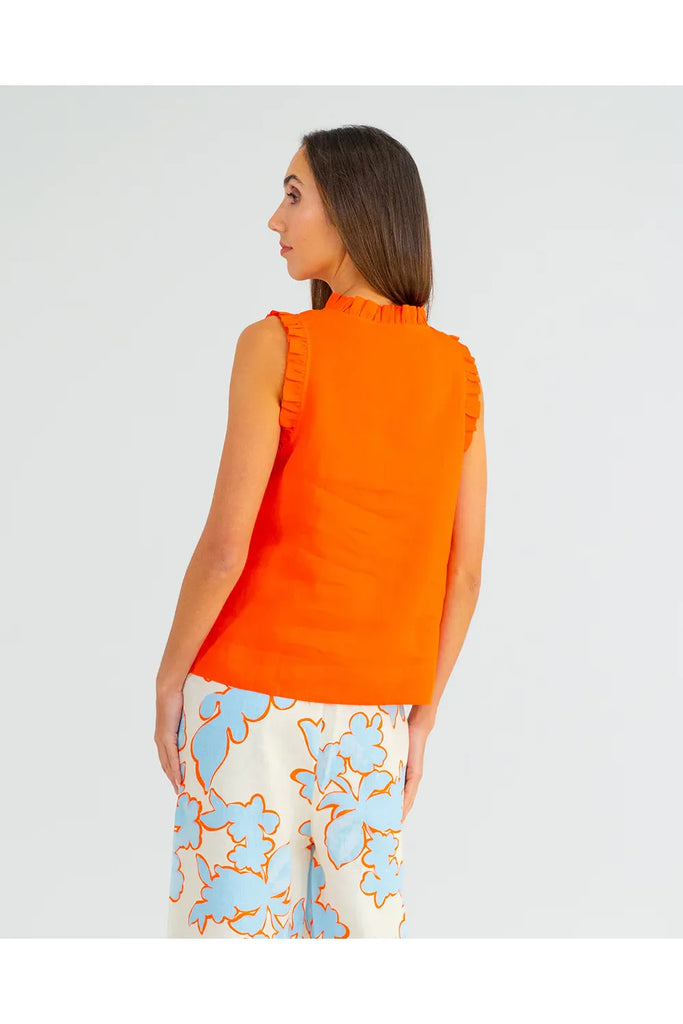 Woman wearing an orange sleeveless top with ruffled details on a plain background. Arlington Milne Lucia Top in Tangerine worn with the Bianca Trouser in Summertime Floral.
