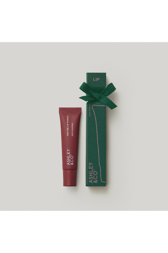 Ashley & Co Forest Collection Tint Me Lip Punch Red Radish. Lip tint with green packaging and bow on a light grey background.