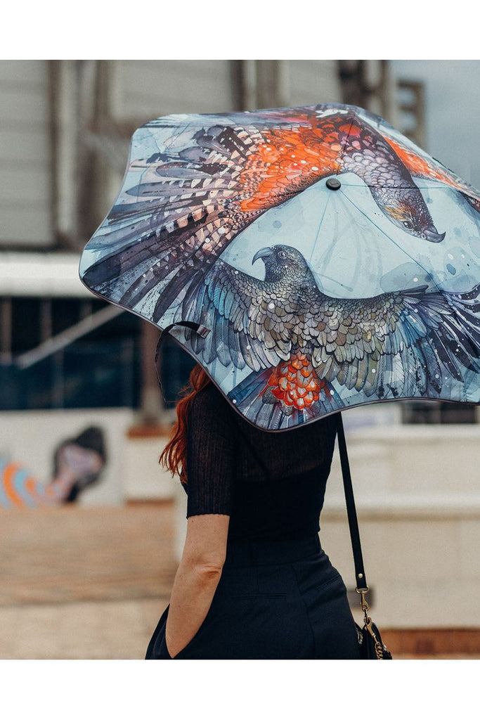 Blunt X Forest & Bird Metro Umbrella featuring a Kea & Kaha Bird Design by Rachel Walker. Photo of Wellington artist Rachel Walker holding the umbrella.  Photo taken from behind so the image on the exterior canopy can be seen.