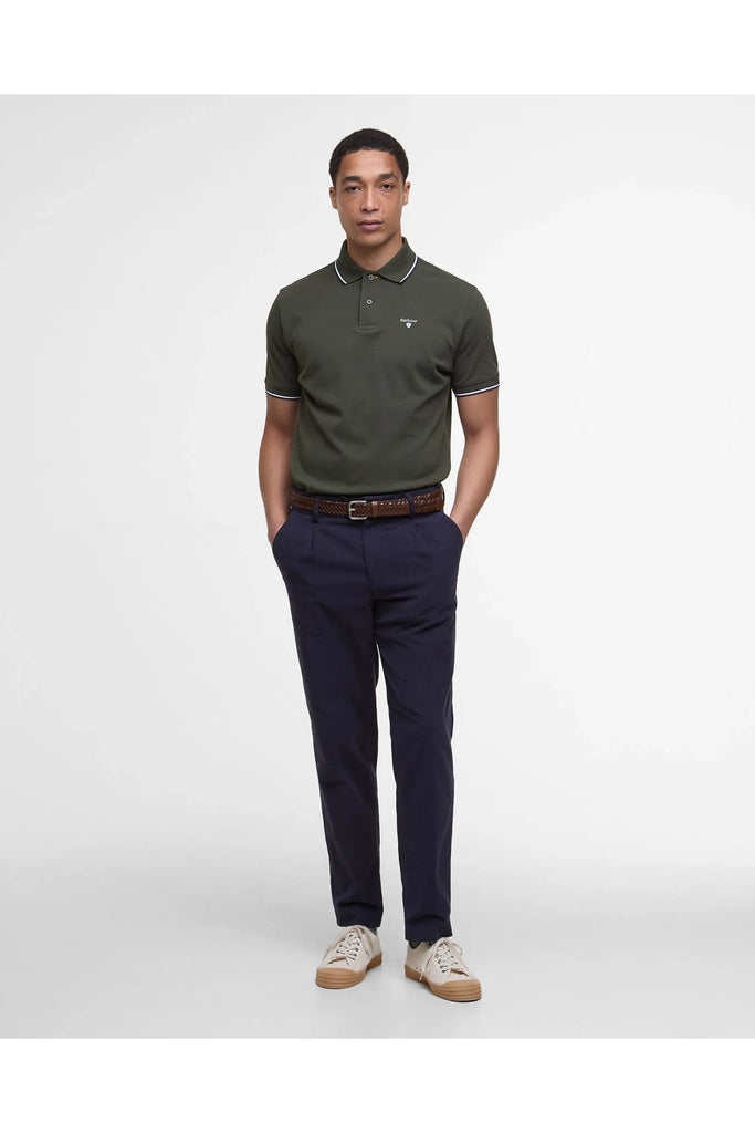 Man wearing the Barbour Fielding Tailored Polo Shirt in Olive with navy blue pants against a grey background