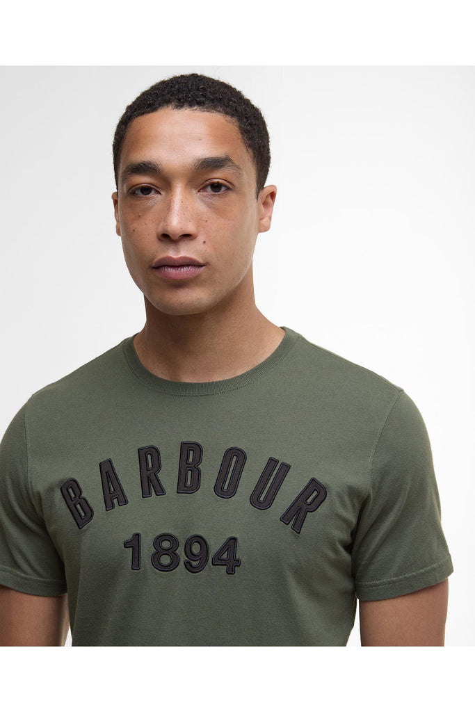 Man wearing a green Barbour t-shirt with 'Barbour 1894' text on a white background. Barbour Hollins Applique T Shirt in Thyme.