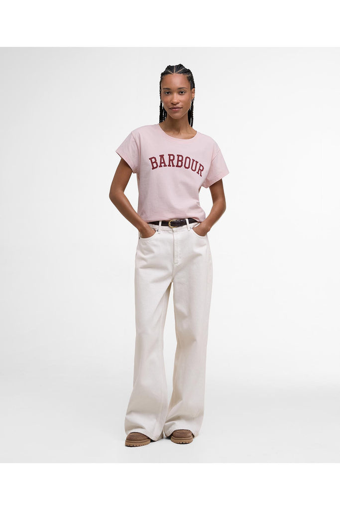 Person wearing a pink 'Barbour' t-shirt and white pants on a white background