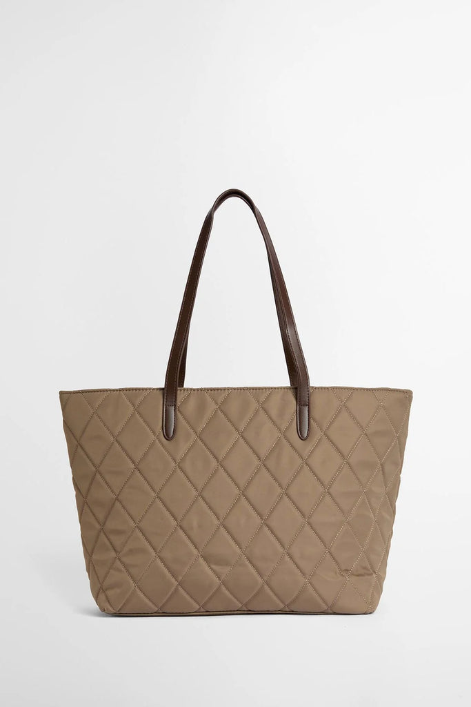 Woman holding a beige quilted handbag against a white background. Barbour Quilted Tote Bag in Sand.