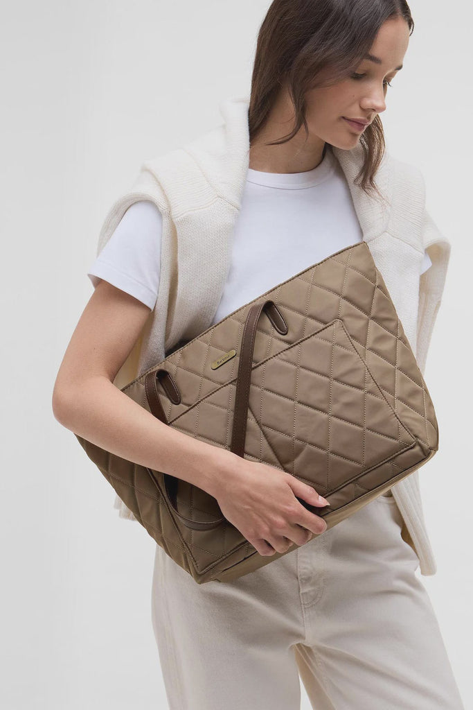 Woman holding a beige quilted handbag against a white background. Barbour Quilted Tote Bag in Sand.