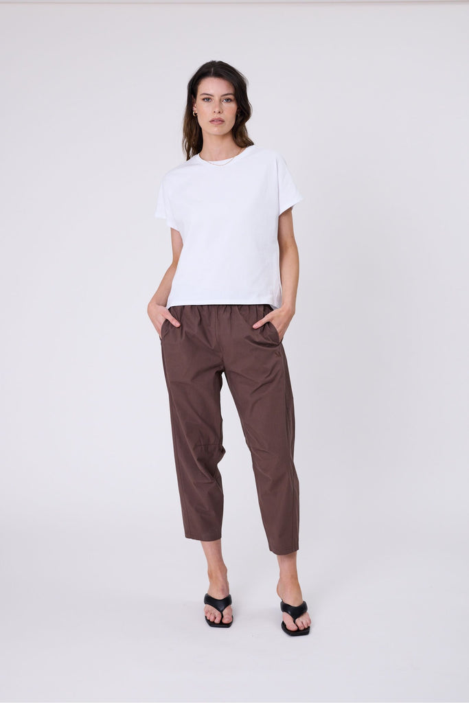 Woman wearing a white t-shirt and brown pants on a white background. Marlow white Barrel Tee.