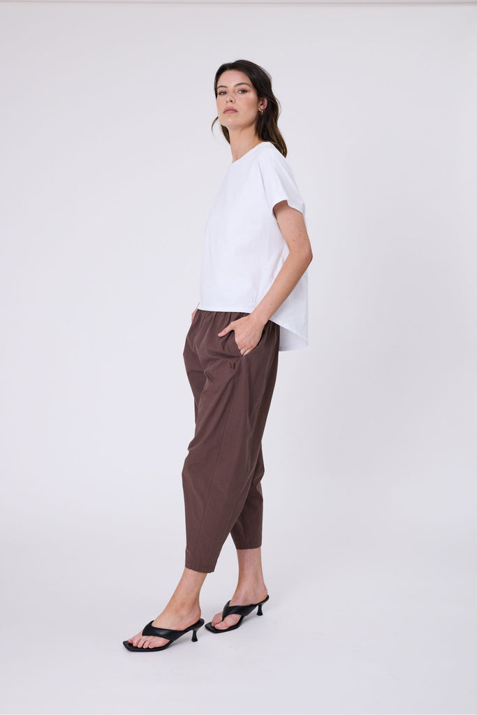 Woman wearing a white t-shirt and brown pants on a white background. Marlow white Barrel Tee.