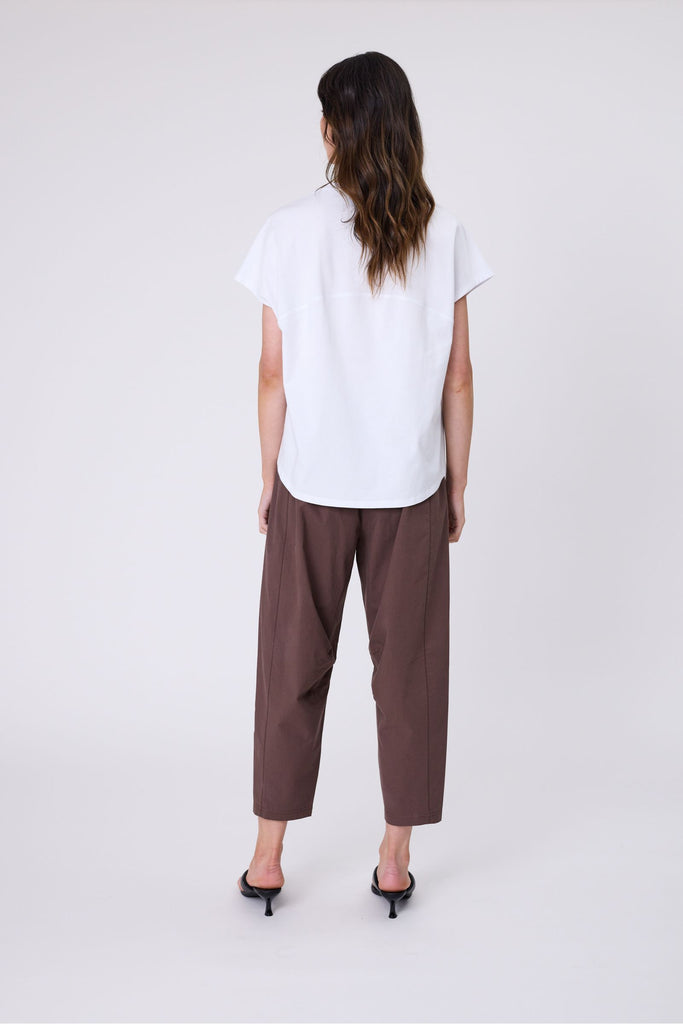 Woman wearing a white t-shirt and brown pants on a white background. Marlow white Barrel Tee.