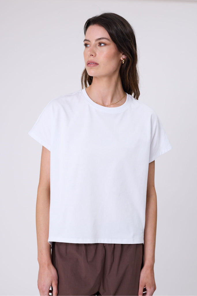 Woman wearing a white t-shirt and brown pants on a white background. Marlow white Barrel Tee.