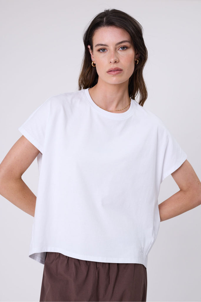 Woman wearing a white t-shirt and brown pants on a white background. Marlow white Barrel Tee.