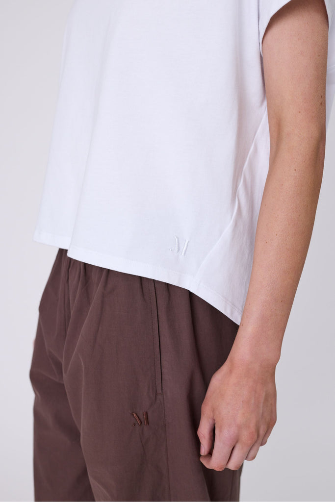 Woman wearing a white t-shirt and brown pants on a white background. Marlow white Barrel Tee.